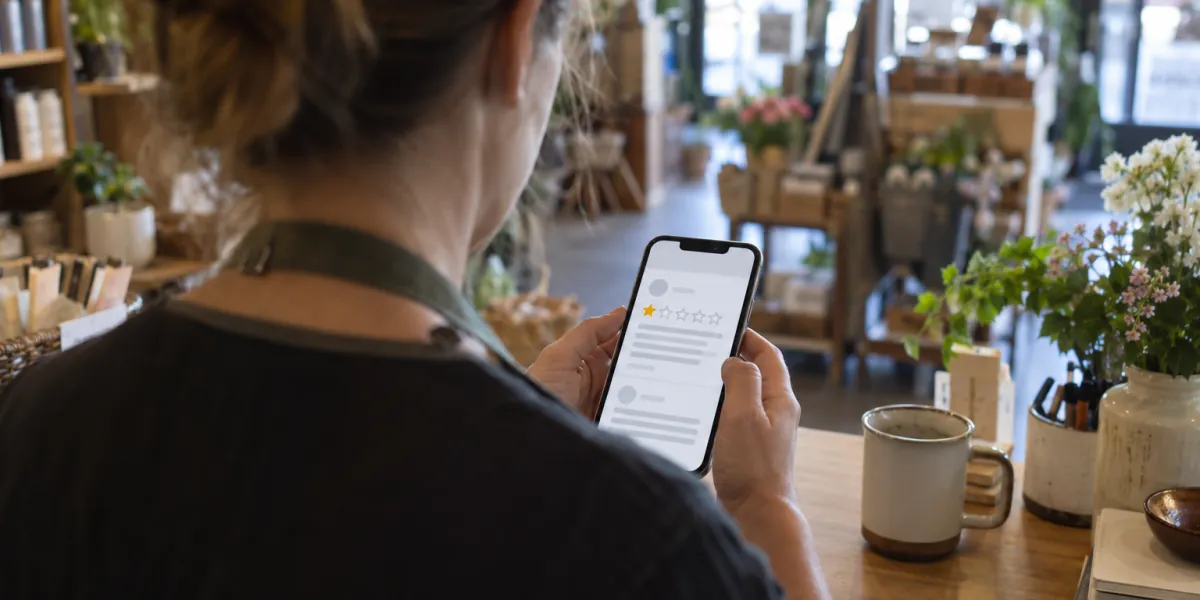 Small business owner looking at a one-star rating on a phone behind the shop counter
